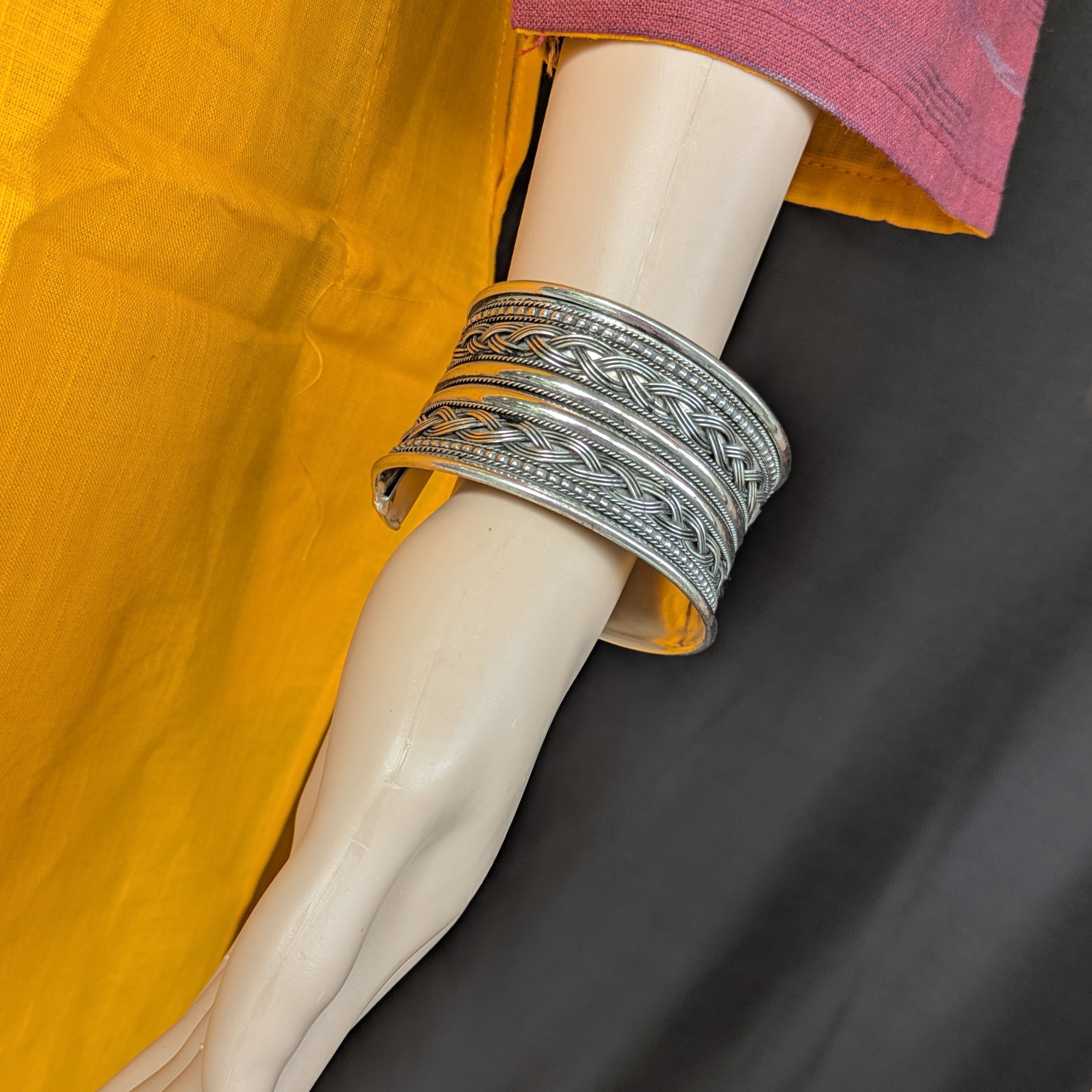 Silver bracelet on a mannequin arm with a yellow garment in the background