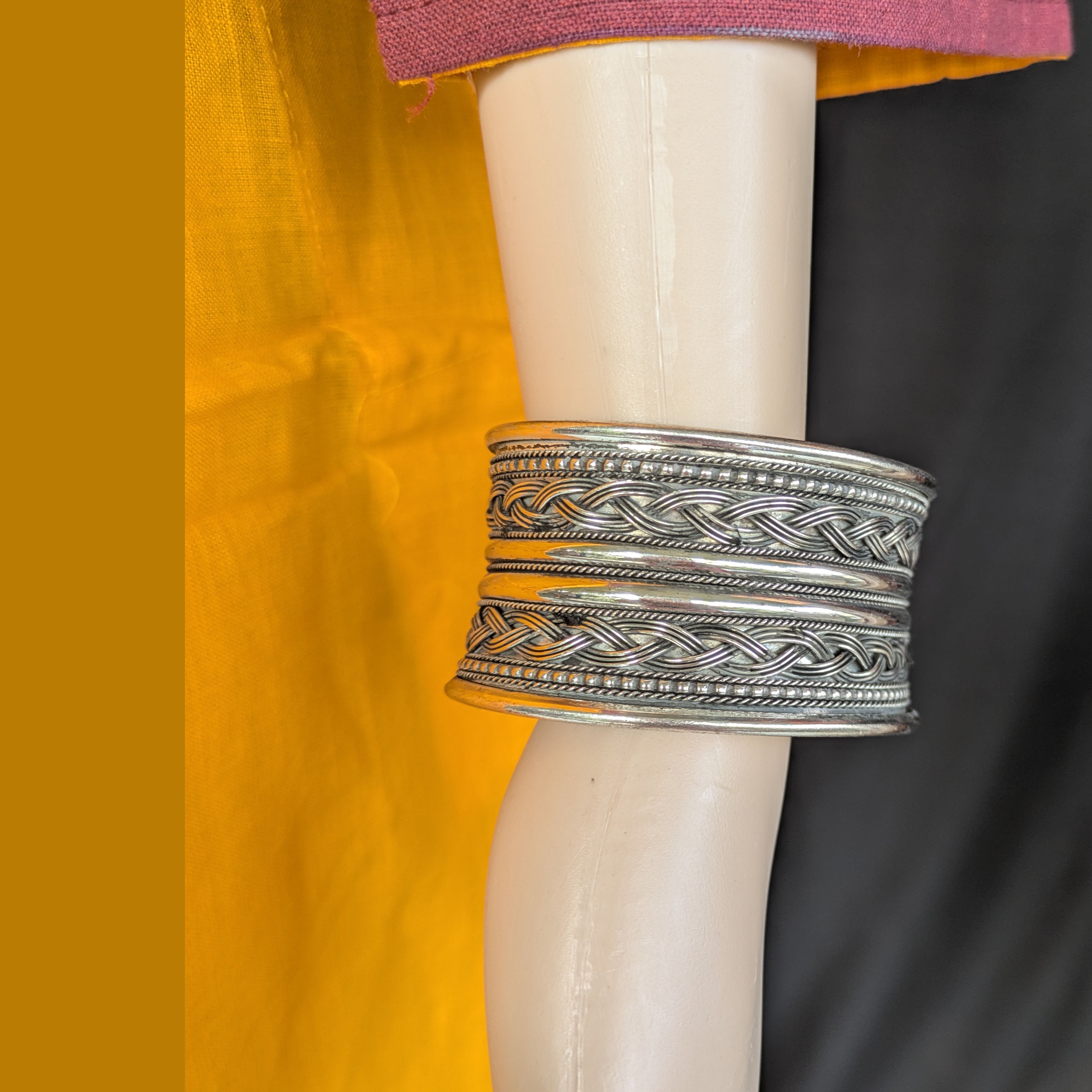 Silver bangle on a mannequin arm with a yellow fabric background