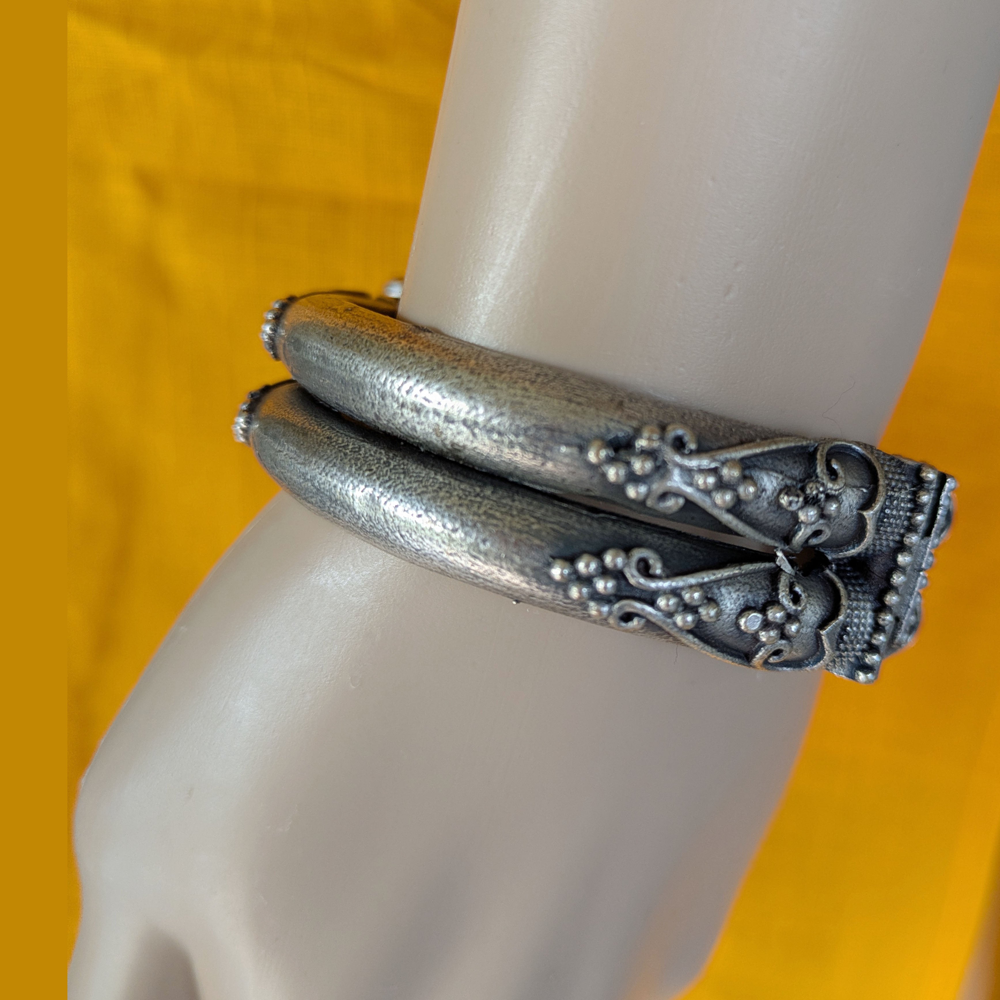 Silver bracelet with intricate design on a mannequin arm against a yellow background
