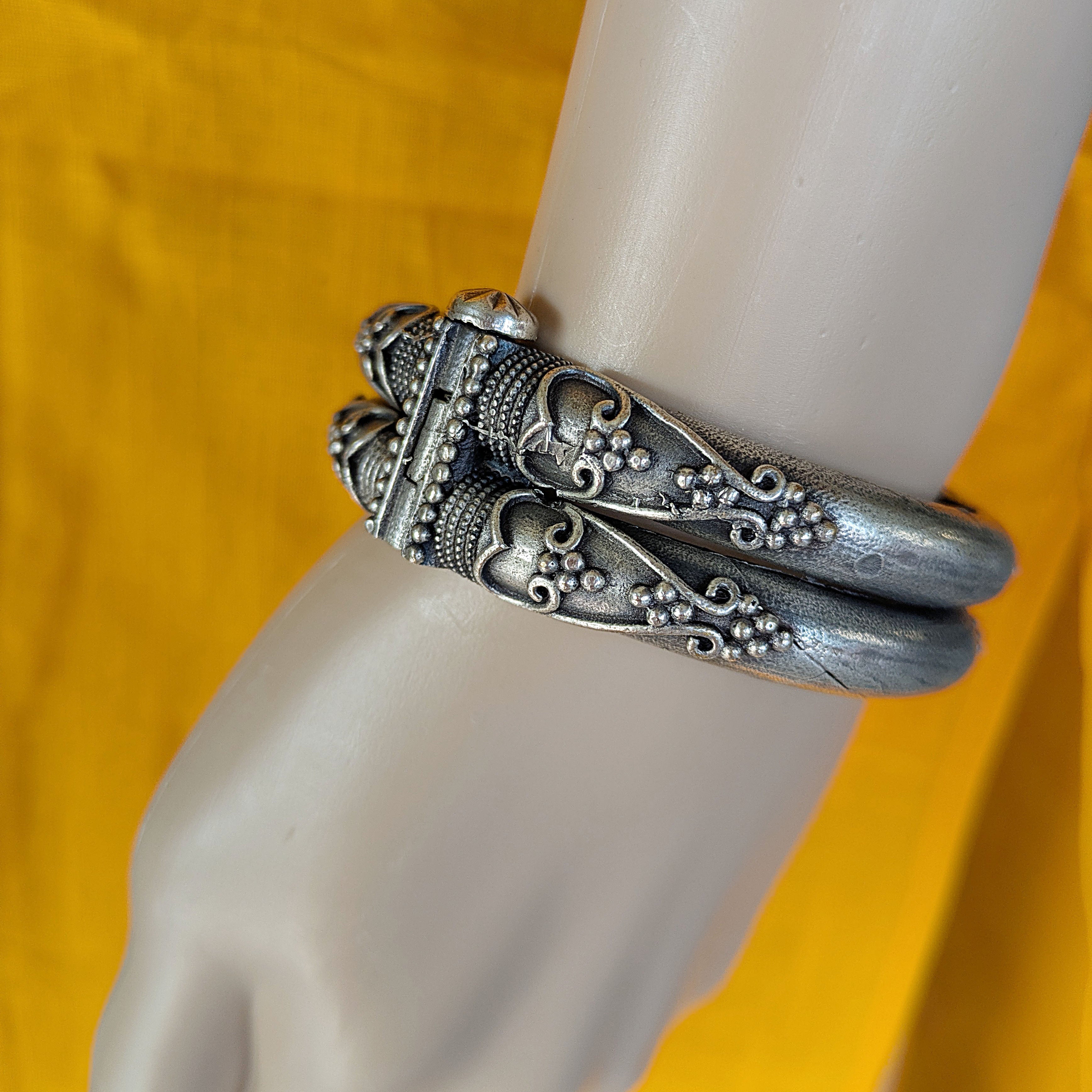 Silver bracelet with intricate designs on a mannequin arm against a yellow background