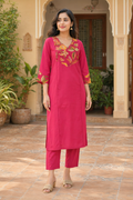 Woman in a pink traditional outfit with floral embroidery standing in a courtyard.