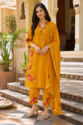 Woman in a yellow traditional outfit with floral patterns standing in front of an architectural structure.