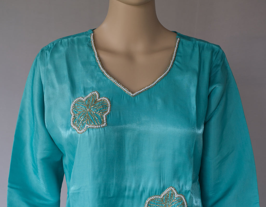 Turquoise blue long-sleeve tunic top with a V-neckline, decorated with silver beaded floral motifs on the chest, displayed on a mannequin torso.
