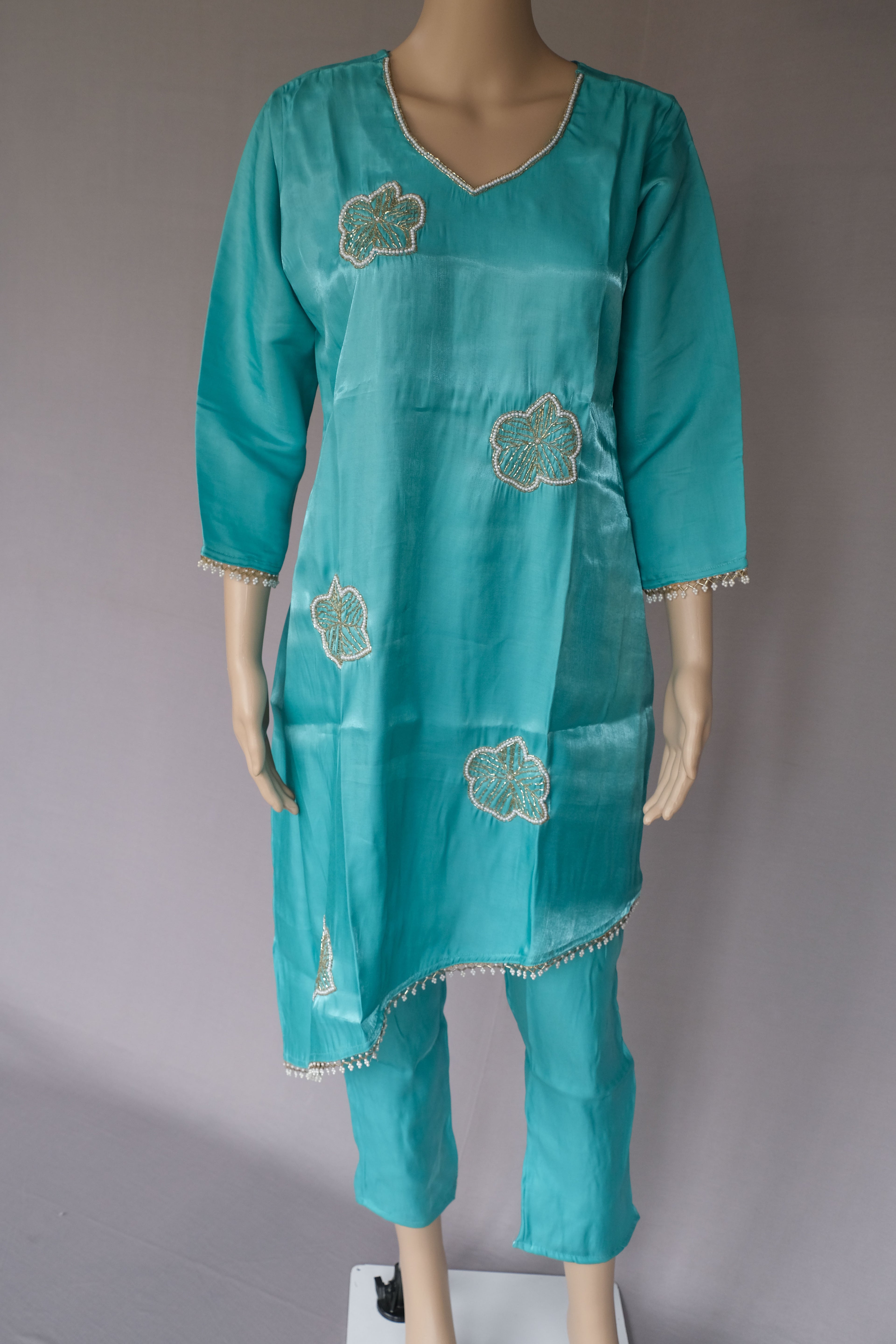 Turquoise blue three-piece kurta set with floral embroidery and silver trim, displayed on a mannequin against a neutral gray background.