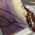Purple and beige woven fabric with a beaded necklace on a white surface