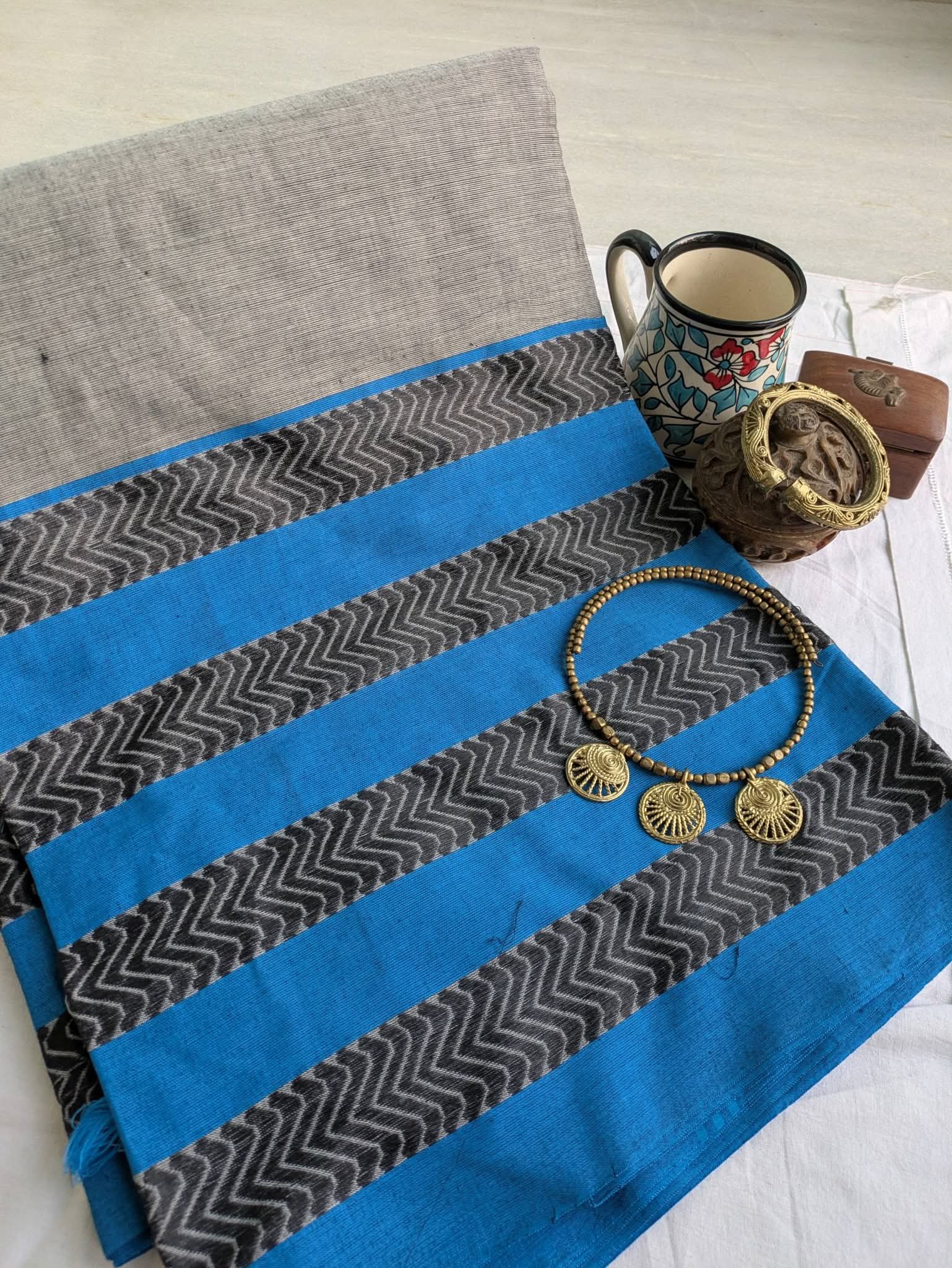 Blue and gray striped fabric with a mug, jewelry, and chocolate on a wooden surface