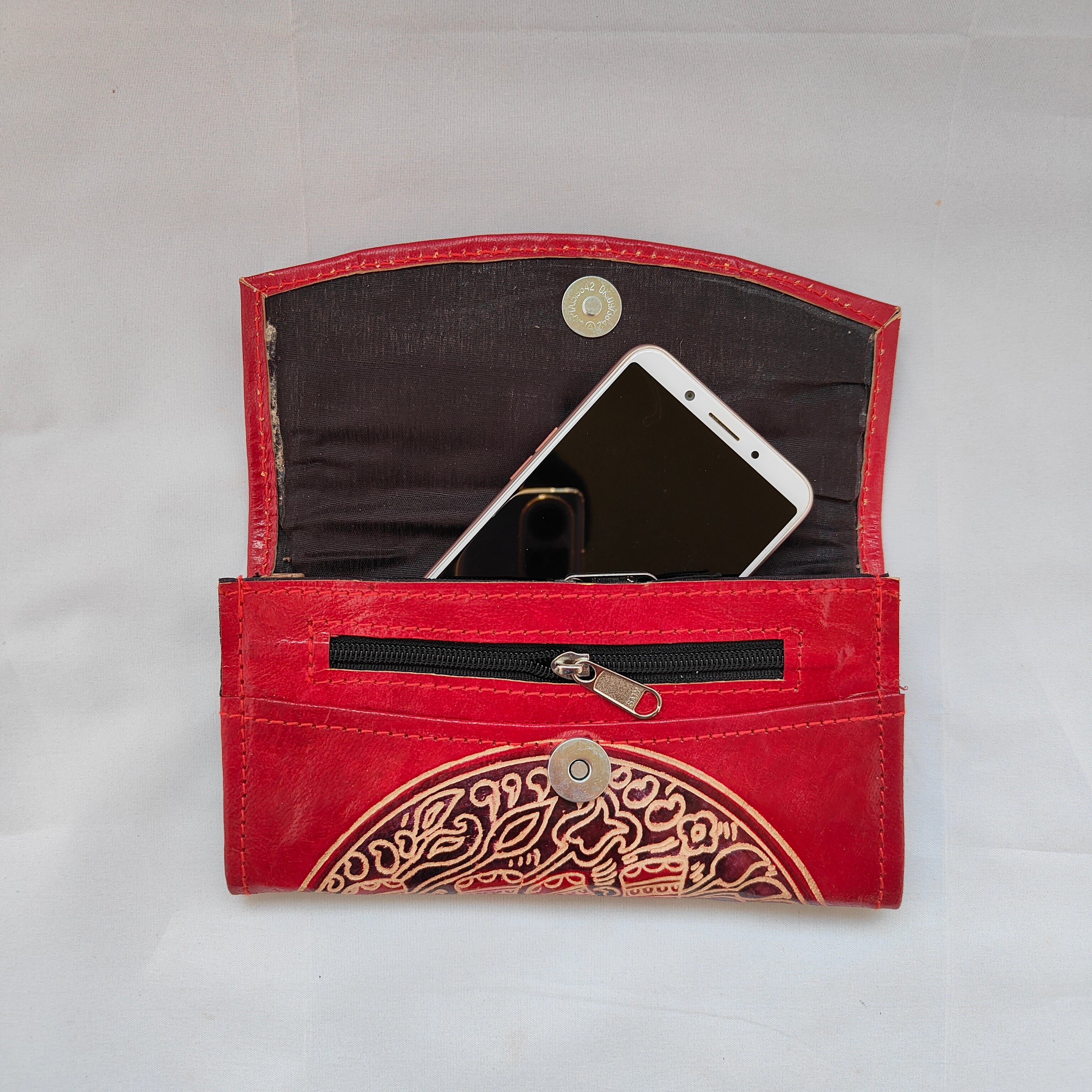 Red wallet with intricate design holding a smartphone on a light gray background