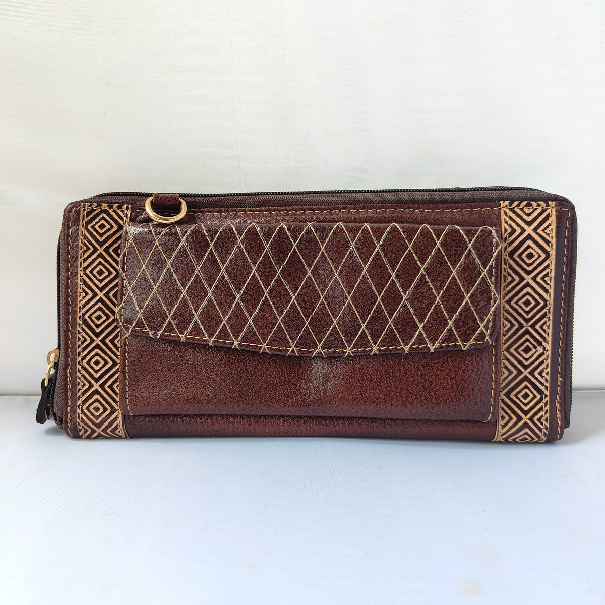 A brown leather zip-around wallet with a diamond-quilted front pocket, gold-tone hardware, and geometric patterned side panels, photographed against a plain light background.