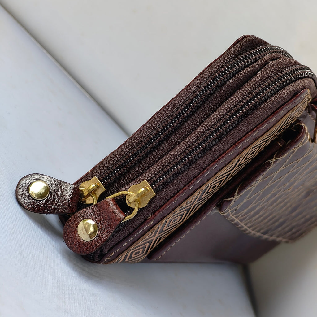 A close-up of a dark brown leather zippered pouch with gold-tone hardware and a textured patterned side panel, resting on a white surface.