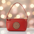 A red leather shoulder bag with a zippered top and a prominent circular gold-toned medallion on the front, set against a plain off-white background.