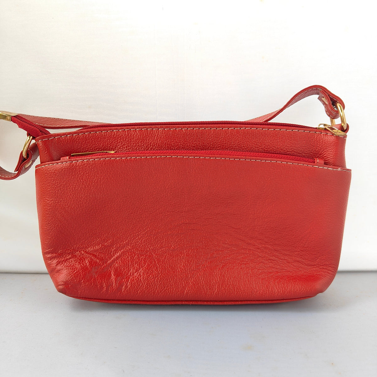 A red leather crossbody bag with gold-tone hardware, shown against a plain white background.