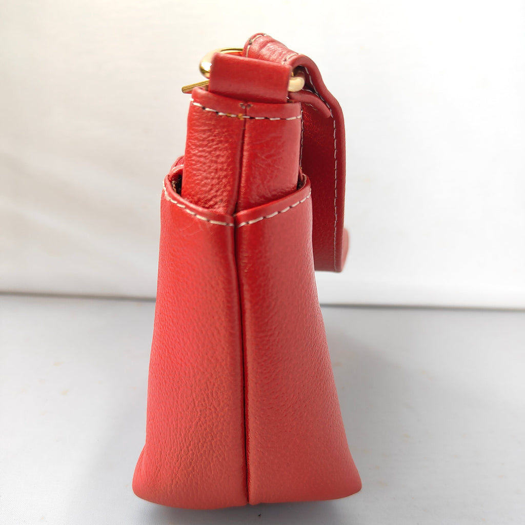 A close-up side view of a red pebbled leather handbag showing the strap attachment and side stitching, set against a plain light background.