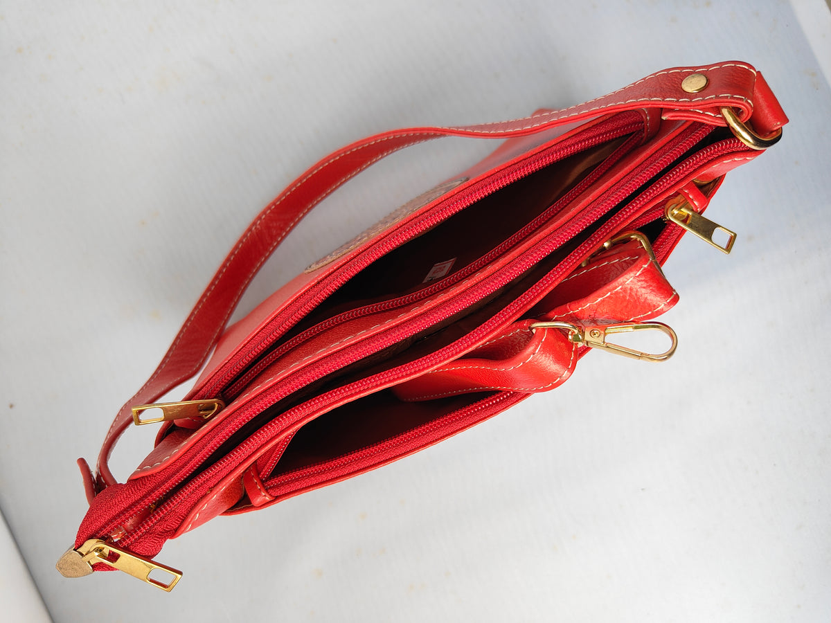 A red leather shoulder bag shown open, displaying its interior compartments and gold-tone hardware, set against a plain off-white background.