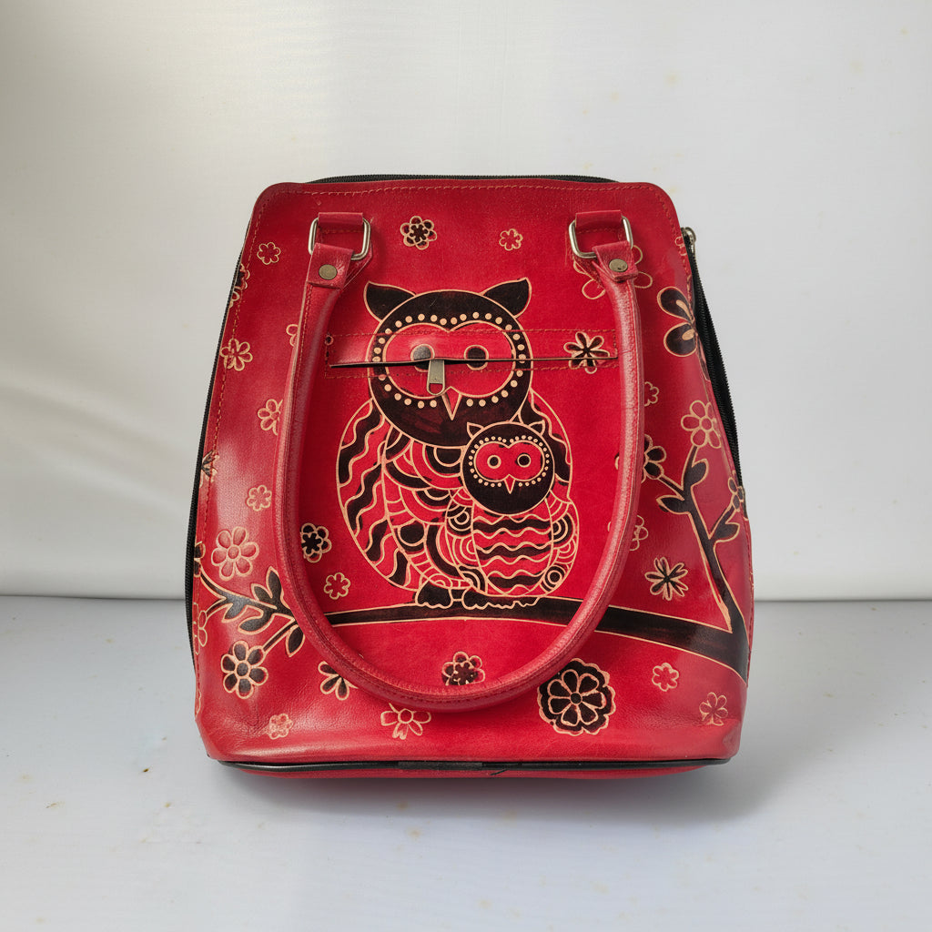 A red leather handbag featuring a large hand-painted owl design in black and red on the front, with floral accents and dual top handles.