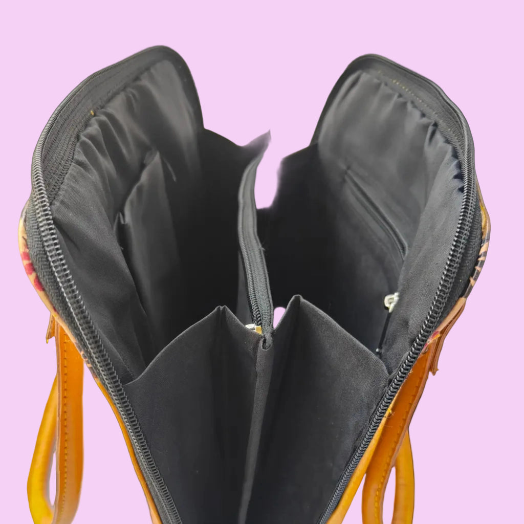 An open yellow and orange patterned handbag showing its black interior compartments, zippers, and lining, photographed against a light background.