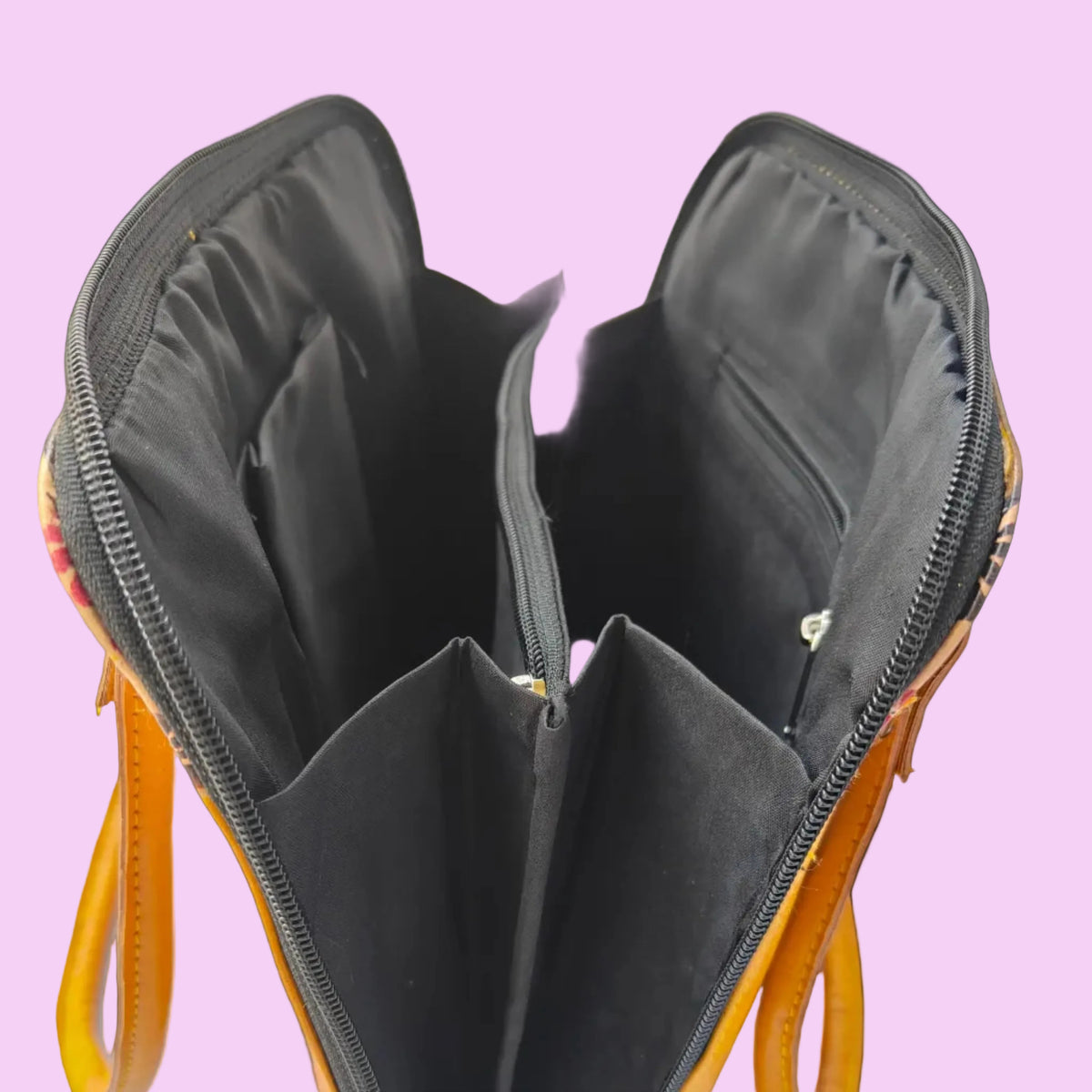 An open yellow and orange patterned handbag showing its black interior compartments, zippers, and lining, photographed against a light background.