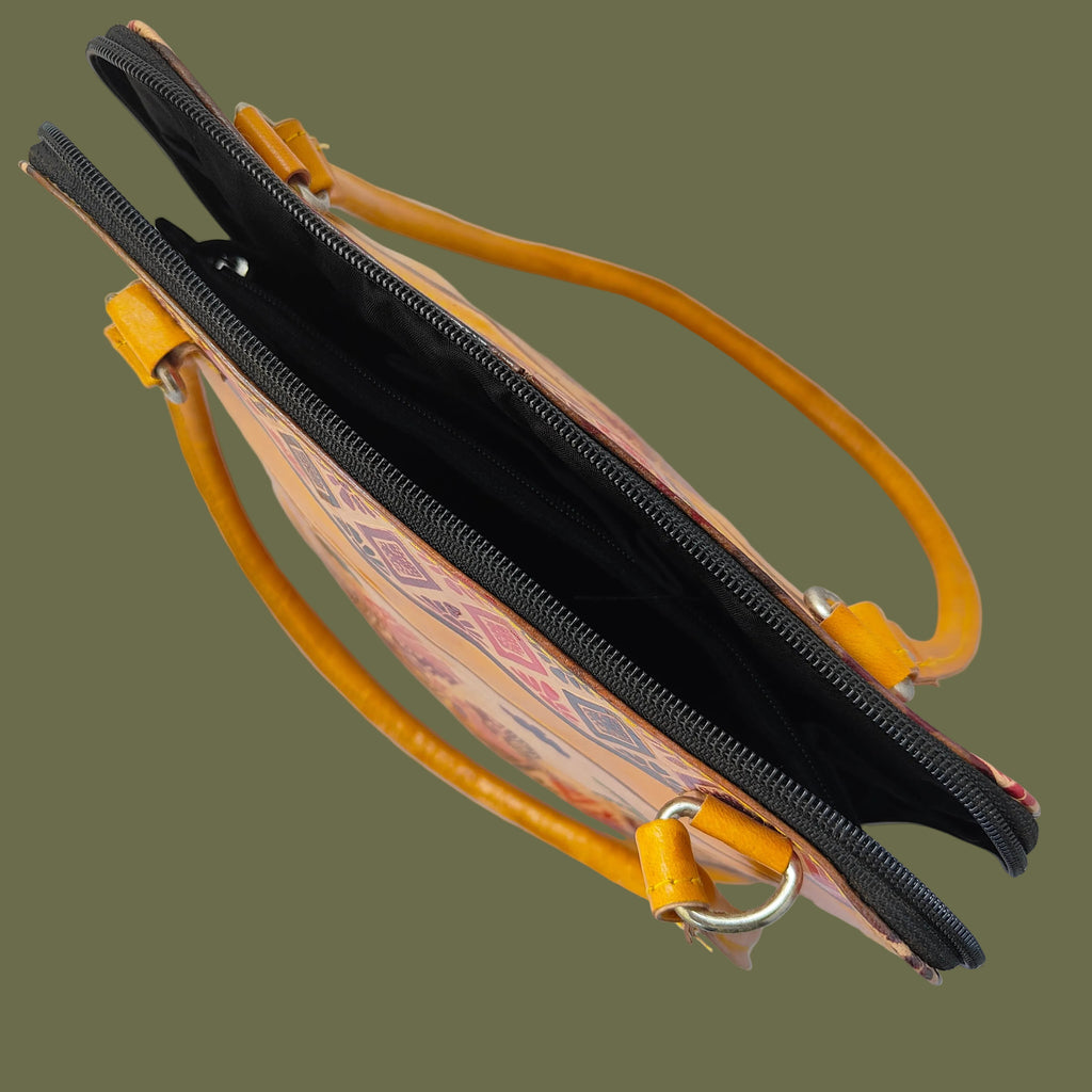 A top-down view of a handbag with a black and orange geometric patterned exterior, a black interior, and bright yellow-orange leather handles and zipper pulls, set against a light gray background.