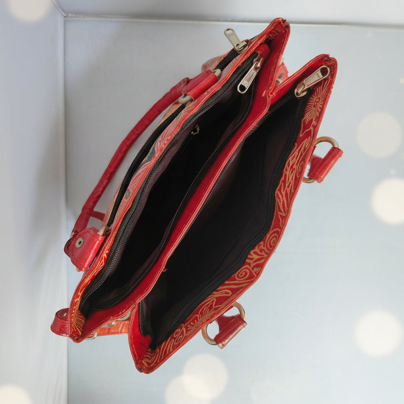 A red leather shoulder bag with gold floral patterns on the exterior, shown open to reveal a black interior and gold-tone zippers.