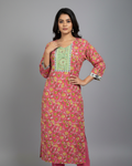A woman modeling a pink printed kurta with a green embroidered yoke and pink pants, standing against a neutral gray studio background.
