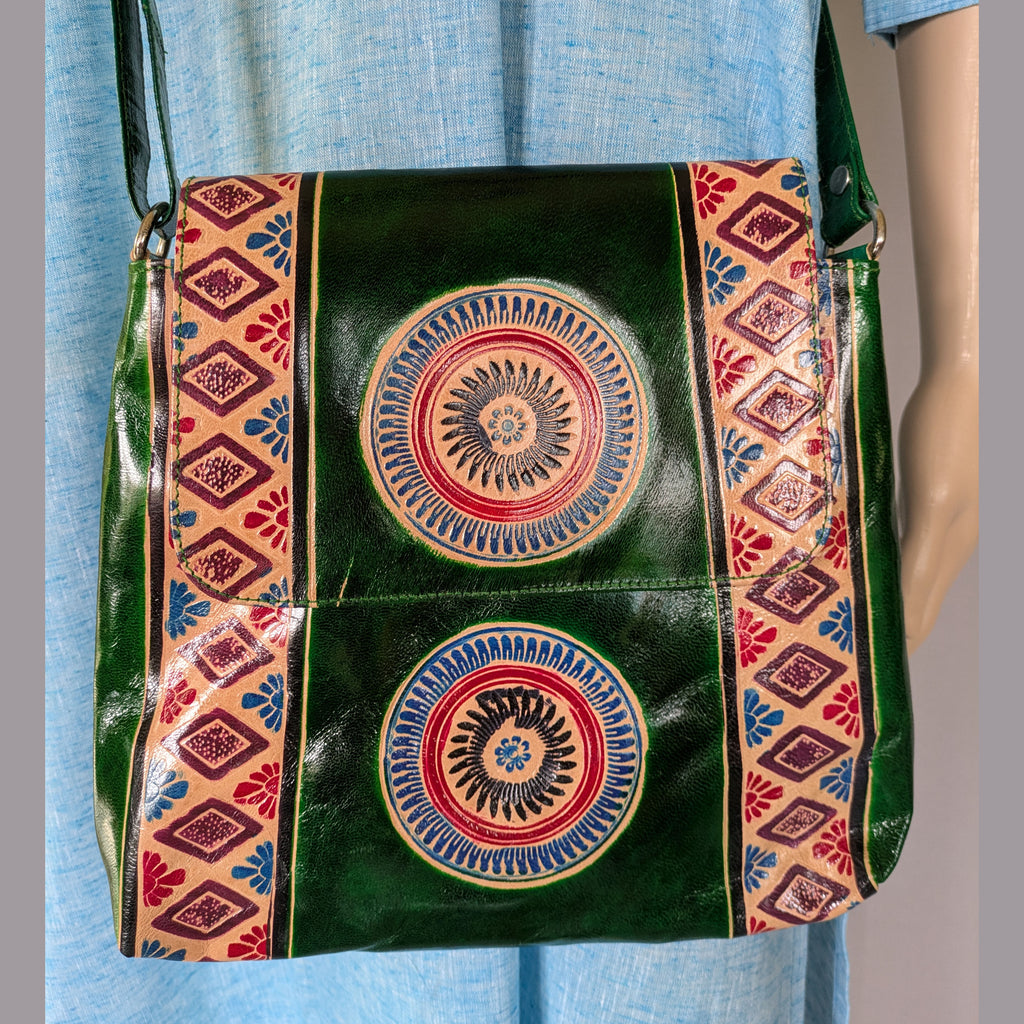 Green leather bag with colorful circular patterns and geometric designs on a blue fabric background.