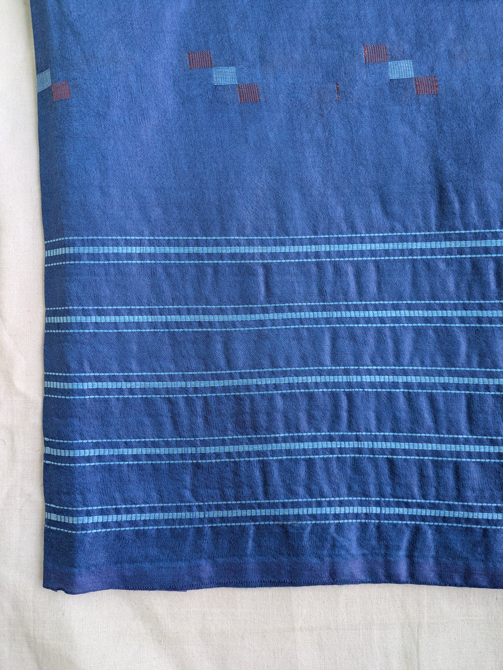 Blue fabric with white stripes and small red and blue square patterns on a white background