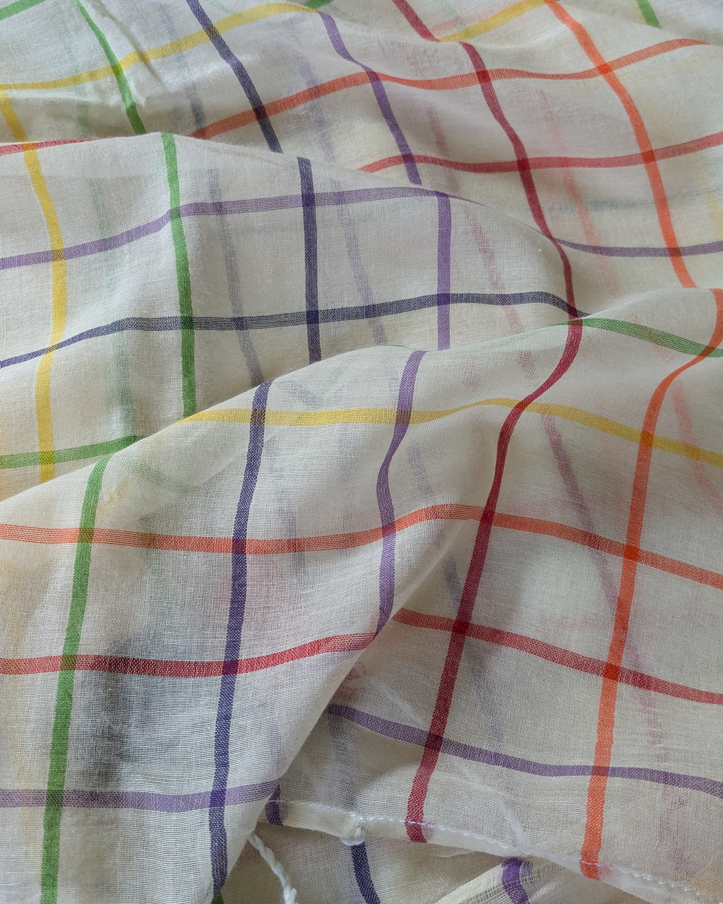 Multicolored checkered fabric with red, green, blue, and yellow lines on a white background.