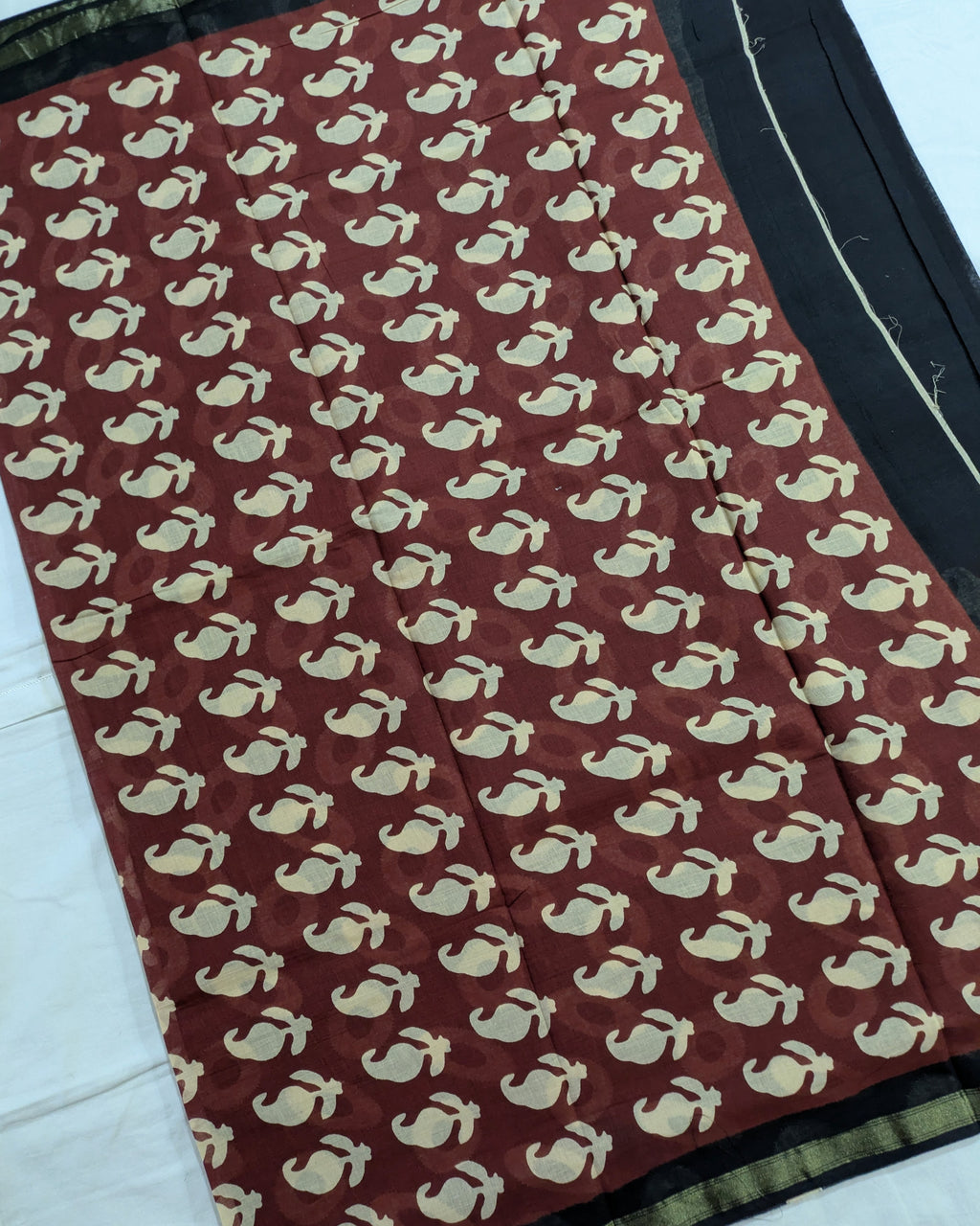 A close-up of a fabric textile with a repeating cream whale or dolphin motif on a deep reddish-brown background, plus a black border with a thin gold stripe along the edge.