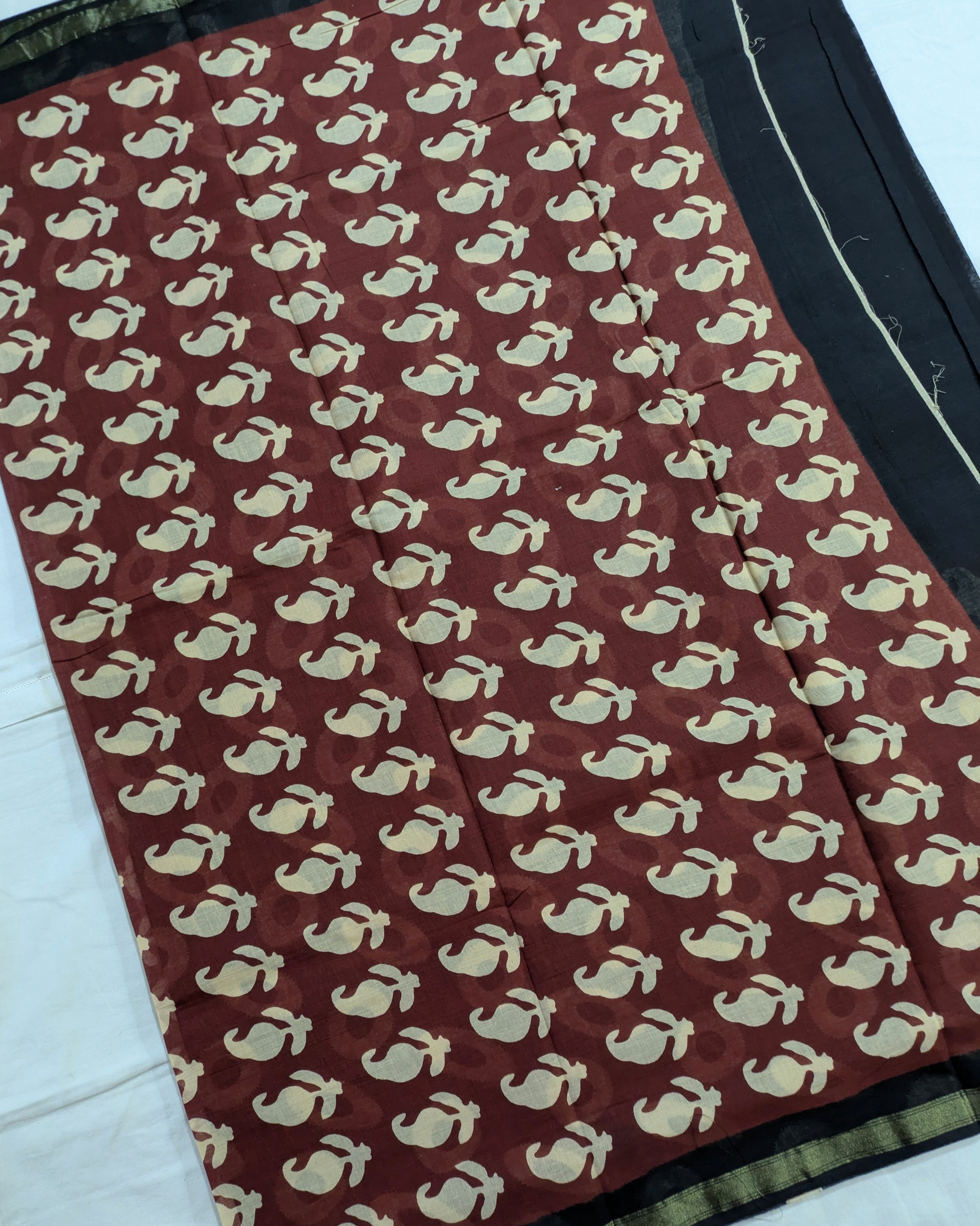 A close-up of a fabric textile with a repeating cream whale or dolphin motif on a deep reddish-brown background, plus a black border with a thin gold stripe along the edge.