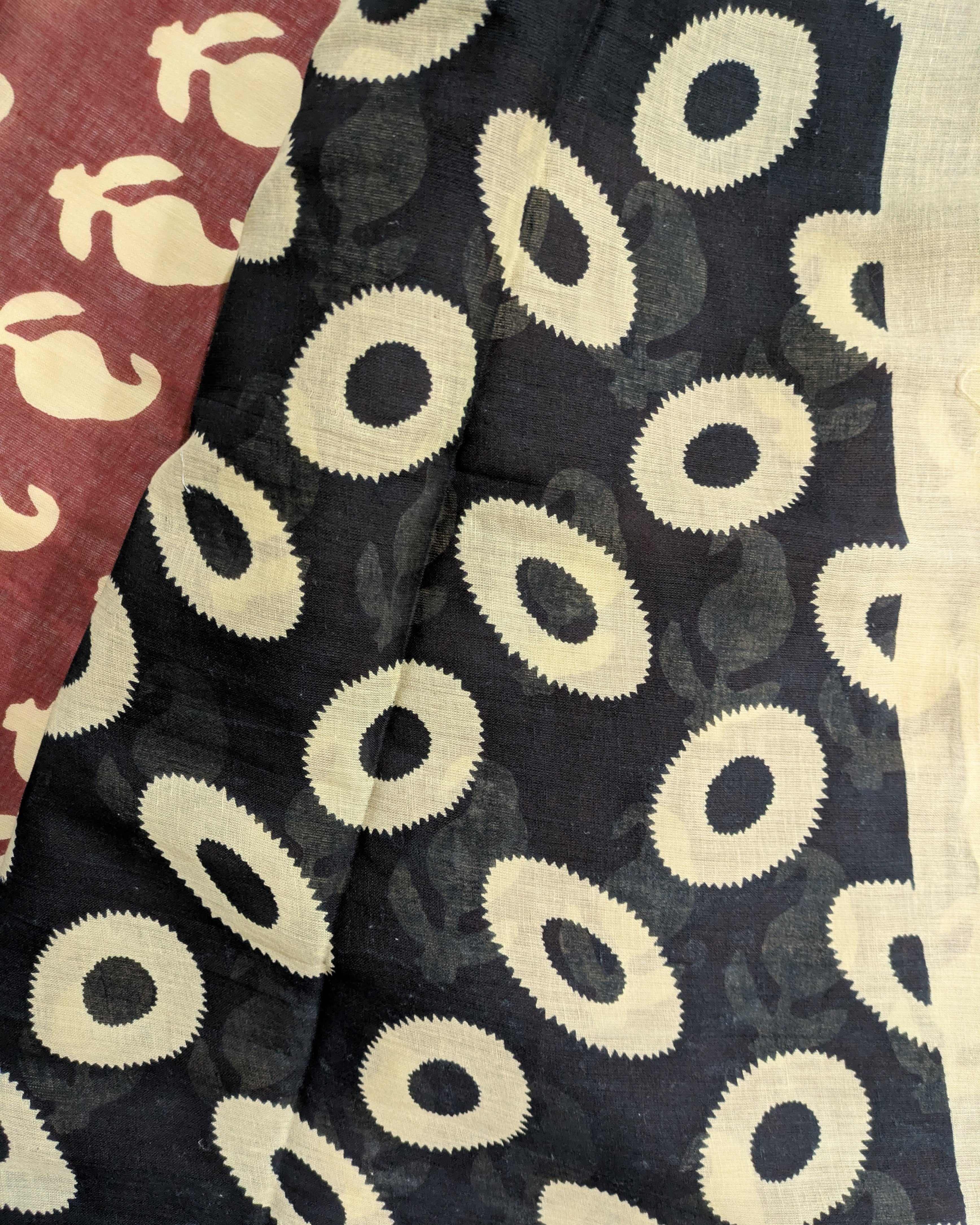 A close-up of a patterned fabric, showing a black section with large cream-colored circular motifs and a maroon section with similar cream motifs.