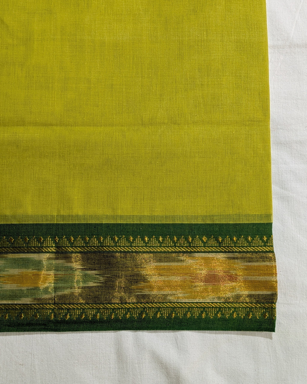 A close-up of a yellow-green fabric, likely a saree pallu or textile panel, featuring a decorative border with green, gold, and brown patterns, laid flat on a white background.