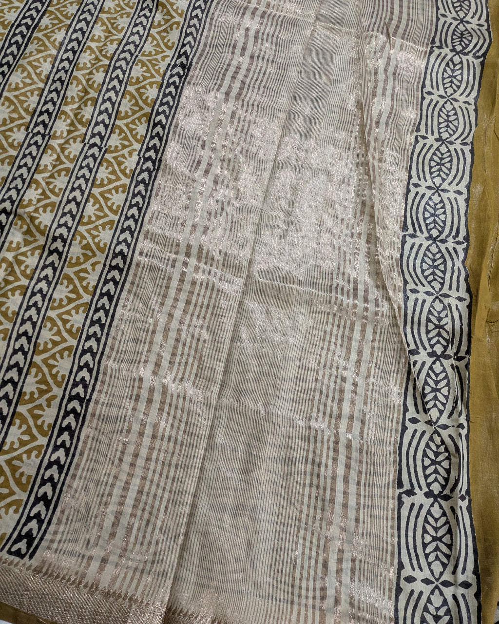 A close-up of a woven textile with a distressed off-white center panel, flanked by a tan patterned section on the left and a black geometric border on the right.