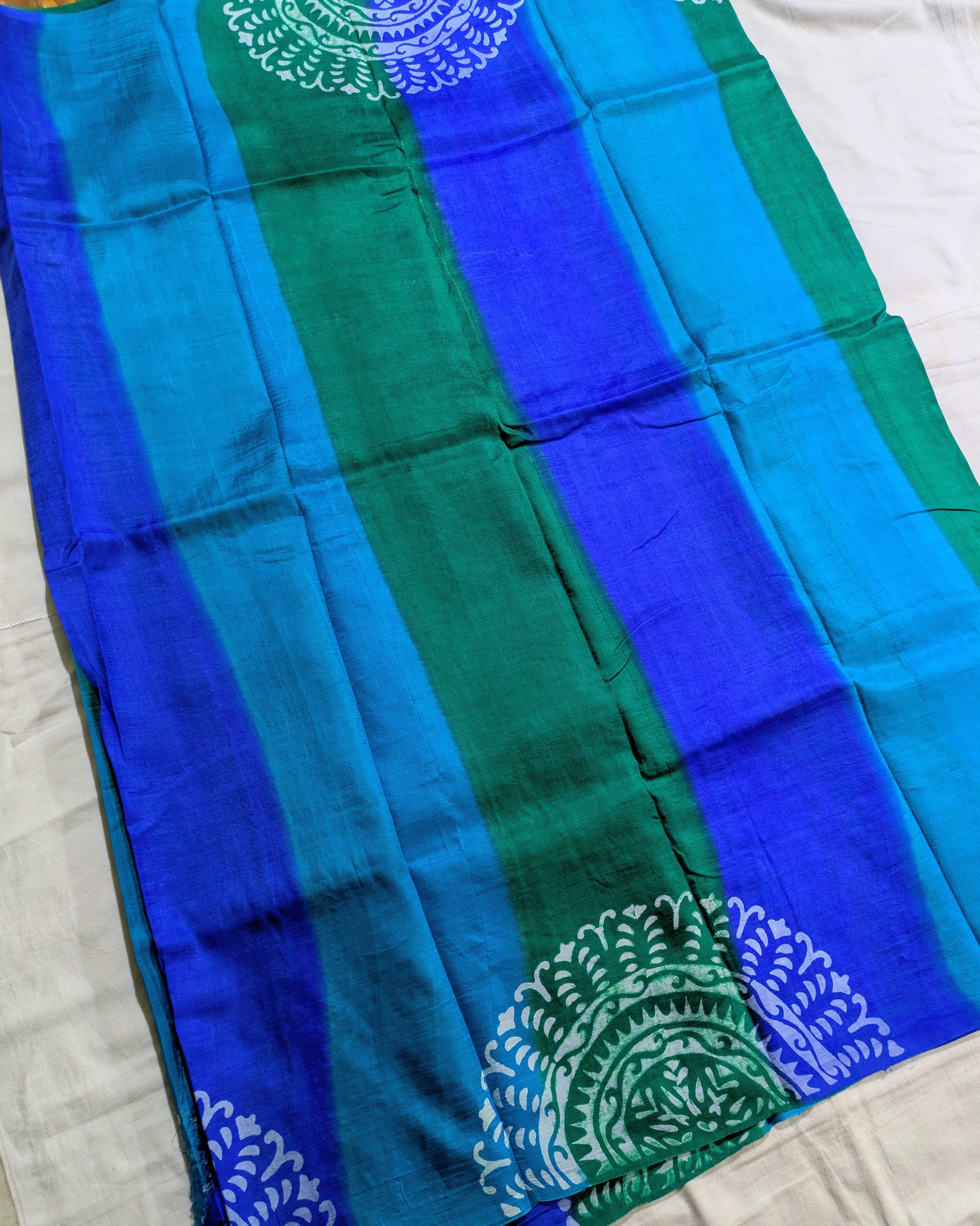 A striped blue and green fabric, likely a saree or scarf, featuring vertical stripes of royal blue, teal, and emerald green with white printed mandala patterns at the corners.