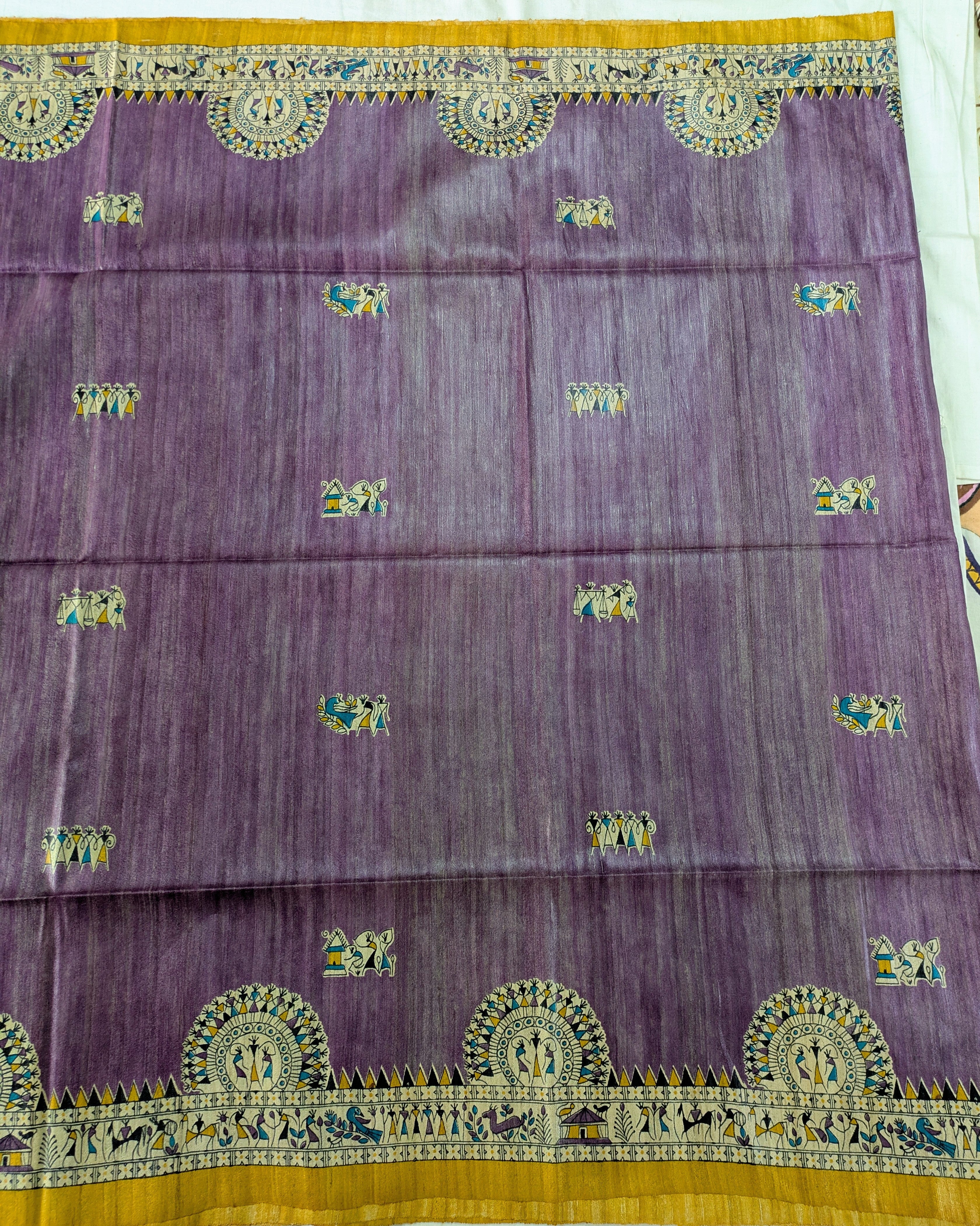 A purple silk saree or fabric panel with intricate gold, green, and blue woven motifs, featuring a wide gold border at the top and bottom.