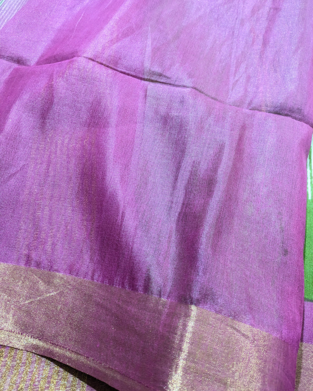 A close-up of a purple silk saree fabric with a shimmering gold border.
