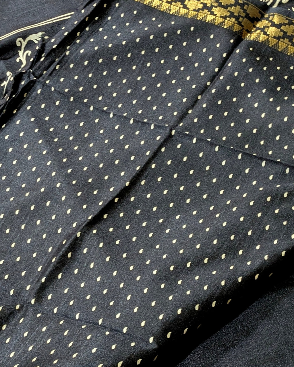 Close-up of a black fabric with a repeating small gold dot pattern and a gold patterned border visible along the top edge.