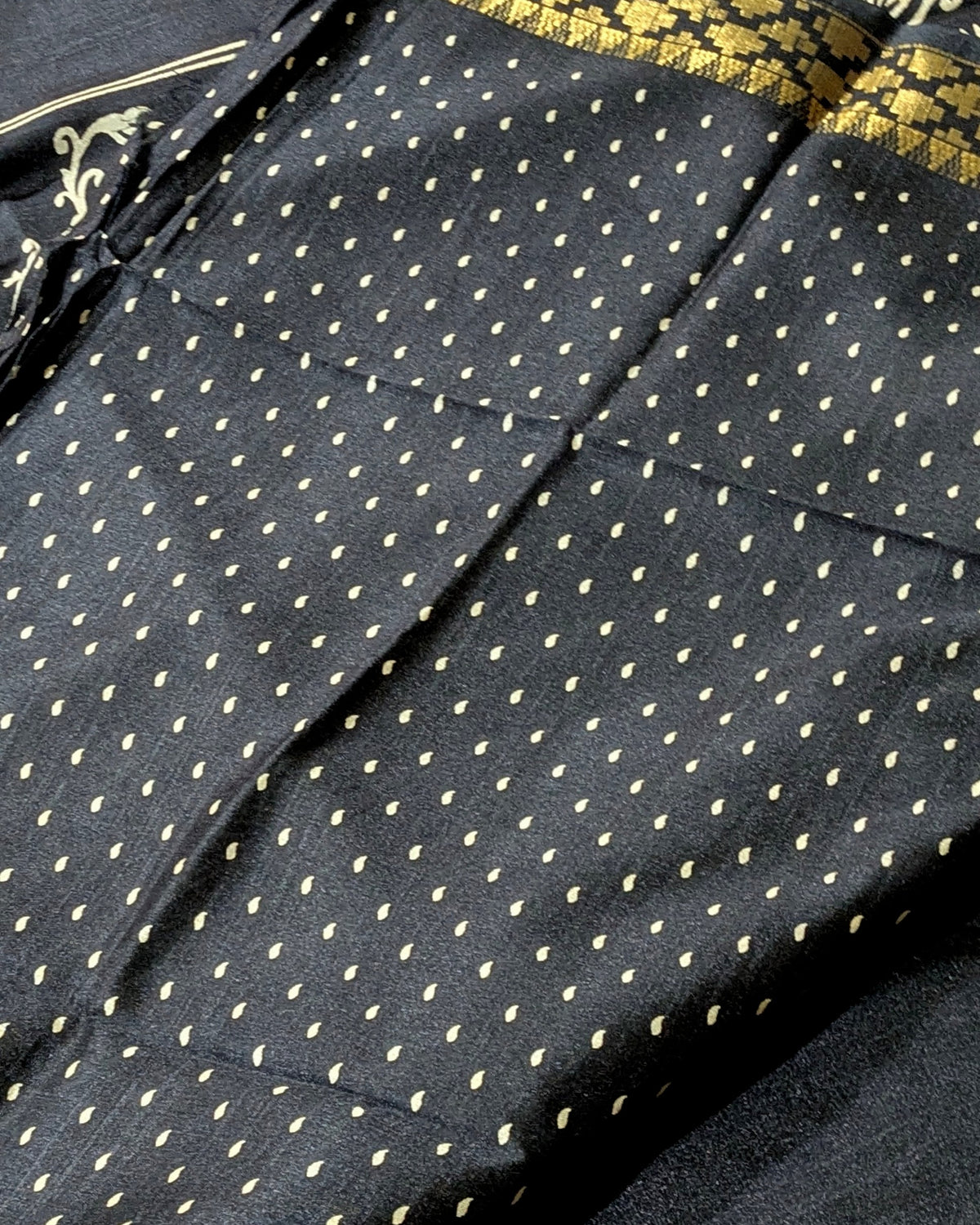 Close-up of a black fabric with a repeating small gold dot pattern and a gold patterned border visible along the top edge.