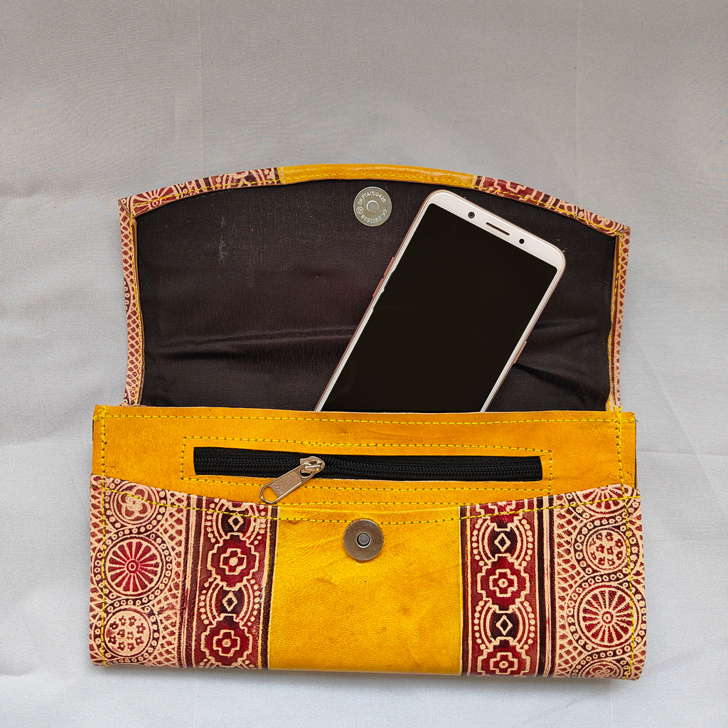 Yellow clutch bag with patterned design containing a smartphone on a light gray background